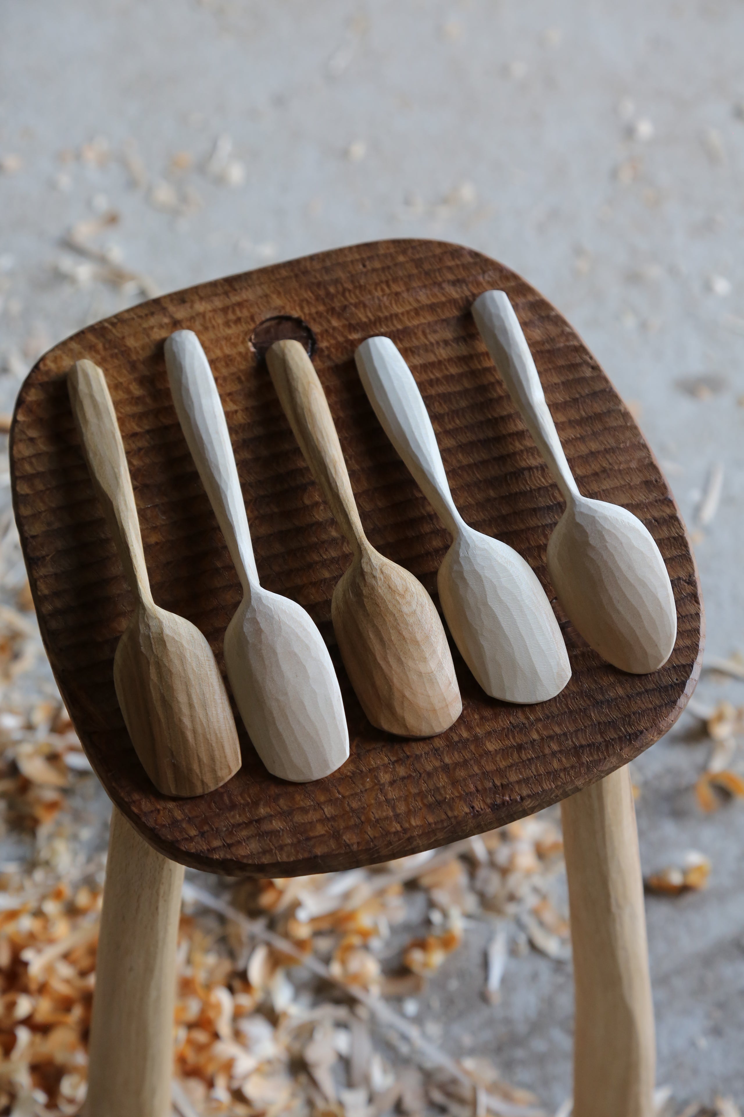 5 wooden eating spoons hand carved from birch and cherry sat on top of a textured oak stool