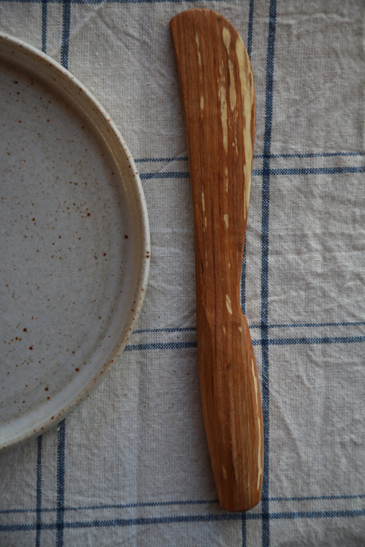Wooden Butter spreader  on a checkered cloth with a ceramic plate in the background