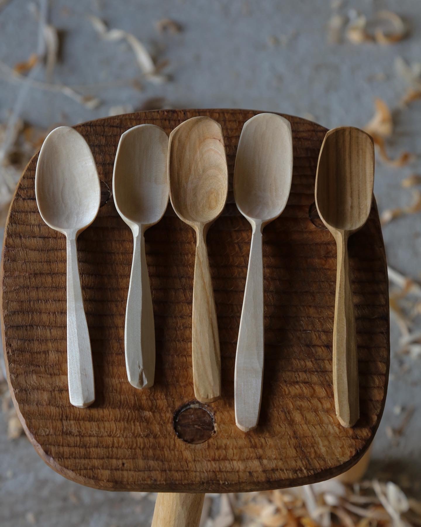 5 wooden eating spoons carved from cherry and birch sat ontop of a textured oak stool 