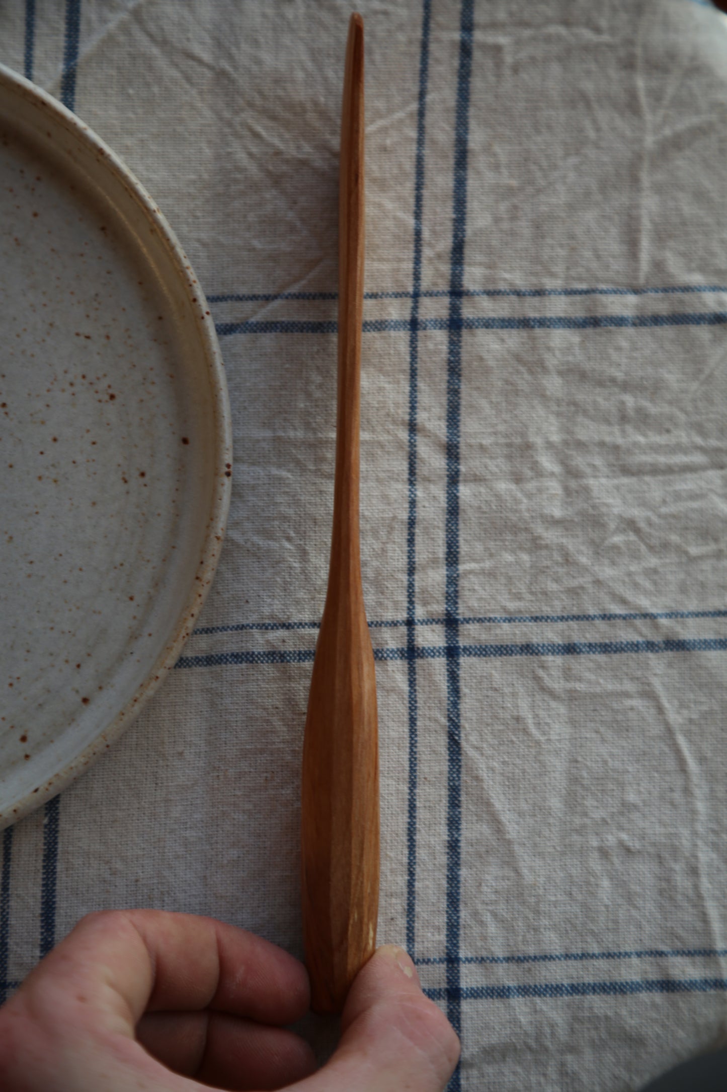 Wooden butter spreader held by a hand on a checkered fabric background